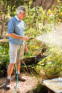快乐的园丁用花园的水管浇水图片