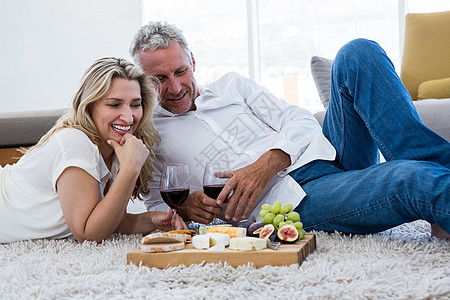 幸福的情侣 躺在地毯上时喝着红酒和食物背景