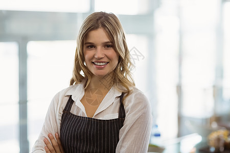 微笑的女服务员站在手举着横穿双手的肖像围裙款待快乐餐厅工作酒店双臂女性咖啡店女士图片