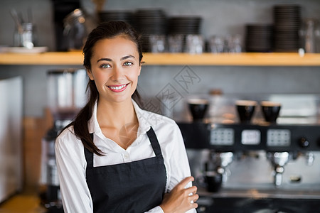 微笑的女服务员站在手举着横穿双手的肖像快乐咖啡店双臂款待围裙酒店女士制服工人服务图片
