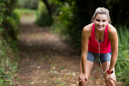 累了的女人在慢跑时休息享受运动服耳机护理腕表娱乐女士听力运动员微笑图片