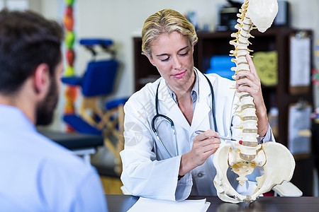 向病人解释脊椎模型的治疗师女性椎骨身体诊所诊断器材桌子男人生理学治疗师背景图片