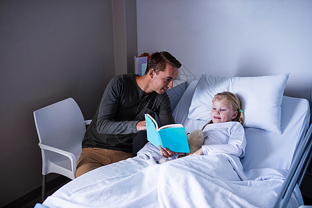 和父亲一起在医院床上读书的女孩疾病病人玩具男性治疗童年服务病床阅读女性图片