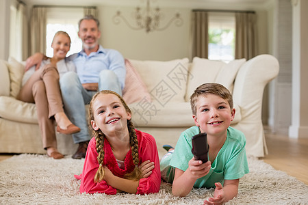 父母和在客厅看电视的小孩享受控制父亲服装乐趣电视母亲喜悦小地毯男生图片