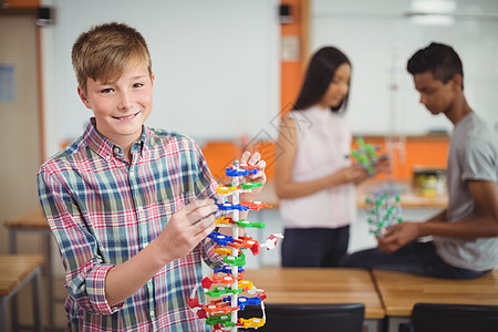 微笑的小学生在实验室检查分子模型的肖像图片