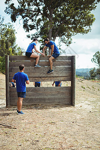 女教练员在障碍课程中协助  健身人  在木墙上爬行娱乐活动男性活力军事运动员力量挑战讲师培训师图片