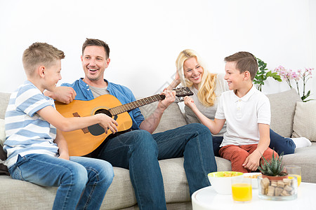 欢乐的caucaosian家庭微笑 在舒适的现代家一起弹吉他和唱歌孩子们妈妈成人男人温暖乐趣沙发女士歌曲童年图片