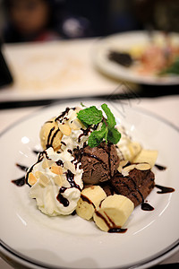 巧克力冰淇淋和香蕉片 用薄荷叶装饰 白色慕斯和杏仁片放在白色盘子里 淋上巧克力酱 看起来很美味 选择性的焦点乡村沙漠奶制品桌子食图片