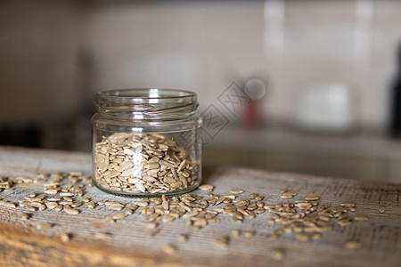 向日葵种子在一个罐子里 种子散落在白色的复古桌子上 背景是厨房 健康的素食蛋白质营养食品 在土气老木头的向日葵种子营养粮食小吃植图片