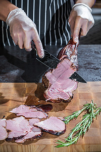 一名厨师将一根烟熏的羊腿切成木板切片午餐迷迭香炙烤烧烤手套美味美食木头餐厅食物图片