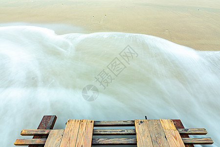 波浪滚滚到沙滩上 木桥底部 长期暴露图片