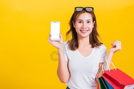 女人微笑 她拿着购物袋和展示手机 她的笑容牙齿女性礼物黄色女士购物者电话销售购物女孩图片