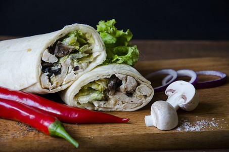 墨西哥食品卷饼配鸡肉 蘑菇 沙拉和酱汁 配红辣椒和切好的蘑菇洋葱 放在蓝色纸背景的木制平台上 与蔬菜和肉类的美味食物图片