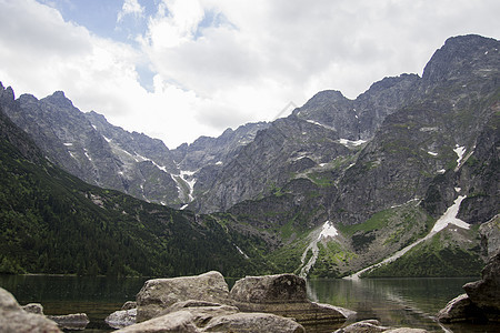美丽的夏季高山湖景被绿树覆盖 前面有石头 天空中有云彩 山在水中的倒影 水晶般清澈的水 欧洲 阿尔卑斯山顶峰场景旅行太阳艺术叶子图片