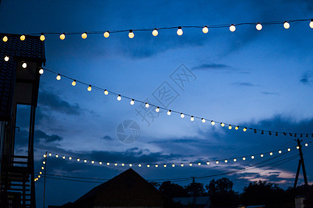 晚上 一排悬挂的夏季露台灯 户外小灯泡力量蓝色金属玻璃树木技术天空细绳活力日落图片
