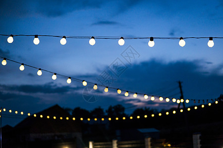 晚上 一排悬挂的夏季露台灯 户外小灯泡活力金属派对细绳花园蓝色技术天空日落玻璃背景图片