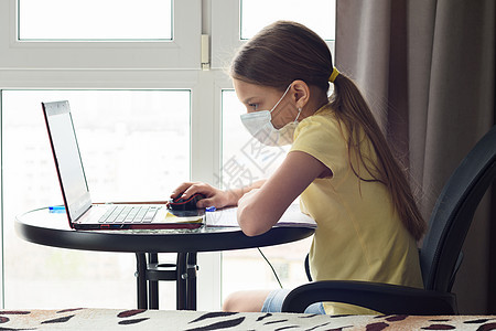 身戴医疗面具的女孩在笔记本电脑上观看在线课程图片