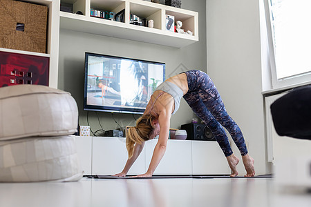有魅力的运动女性在家锻炼 在客厅的电视机前做普拉提运动 社交隔离 在冠状病毒大流行期间保持健康并待在家里地面身体瑜伽娱乐程序女孩图片