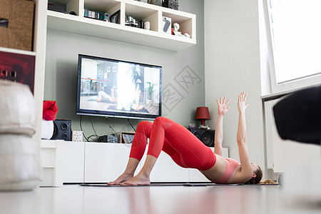有魅力的运动女性在家锻炼 在她的小工作室公寓里在电视机前做普拉提运动 社交隔离 在冠状病毒大流行期间保持健康并待在家里运动装程序图片