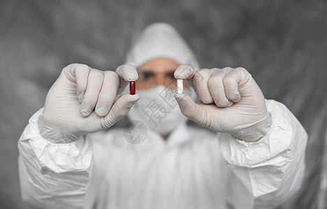 身穿白色防护服 医用口罩和橡胶手套的医生拿着一颗红白相间的药丸 作为应对冠状病毒大流行病威胁的药物 冠状病毒covid 19的流图片