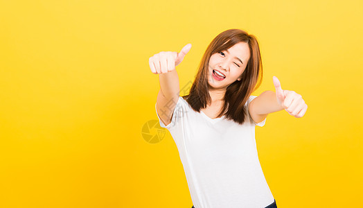 女青少年站着穿T恤衫 佩戴手指拇指白色黄色女孩手势牙齿女性成人商业工作室女士图片