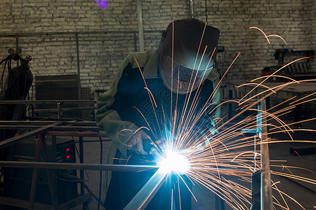 焊工在工业环境中焊接金属部分 并佩戴标准防护设备SDA建造生产蓝色职业制造业修理技术火花安全工匠图片