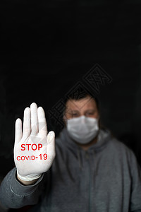 戴医疗面具和手套的男子用手展示“停止行动” 红色文字在黑暗背景中阻止CARVID 19 科罗纳病毒感染保护概念图片