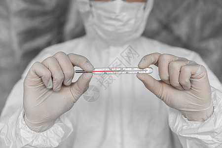 穿着白色防护服 医用口罩和橡胶手套的医生拿着冠状病毒流行病的温度计 流行病 冠状病毒 covid 19 的流行病 测量和指示温度图片