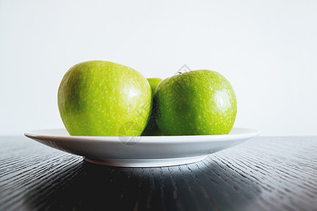 白色盘子上三个新鲜的绿苹果图片