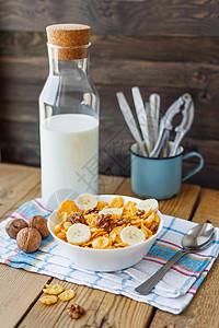 美味的玉米薄片 有胡桃和香蕉 碗里还有奶瓶 铁质木本底和格子餐巾 健康的脆饼早餐点心图片