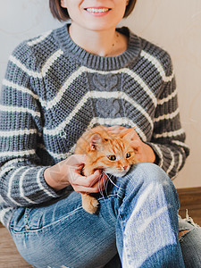 可爱的姜猫跪在女人的膝盖上 笑着的女人被撕破牛仔裤打得屁滚尿流的宠物毛衣乐趣毛皮瞌睡猫科动物哺乳动物微笑拥抱女士女性图片