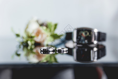 一对金色结婚戒指 光滑镜面镶有钻石 背景上有一朵玫瑰花和一块手表的胸花 婚礼上新郎的传统配饰图片
