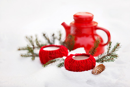 红杯装在编织的罩子和雪中的水壶里 冬天野餐图片