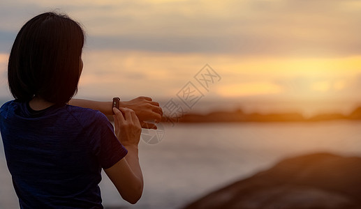 背对背看亚洲女人在跑步后触摸智能乐队图片