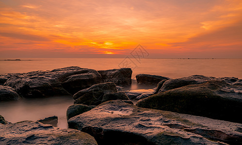 日落时在石滩上的岩石 美丽的海滩夕阳天空阳光戏剧性橙子海景支撑崎岖石头假期海岸旅行图片