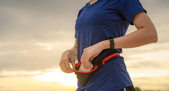 年轻亚洲女性在跑步前用腰包装智能手机手腕活动锻炼技术手表慢跑者女孩速度日出教练图片