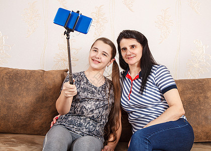 妈妈和女儿用智能手机带自拍照片乐趣电话家庭女性拍照快乐相机母亲沙发图片