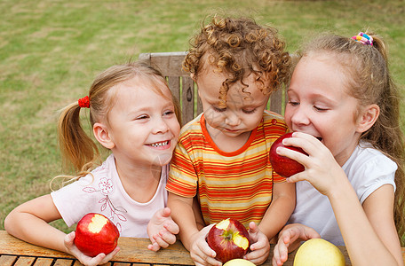 三个快乐的孩子坐在桌边吃苹果 坐着吃饭乐趣花园公园营养女性头发水果食物童年男生图片