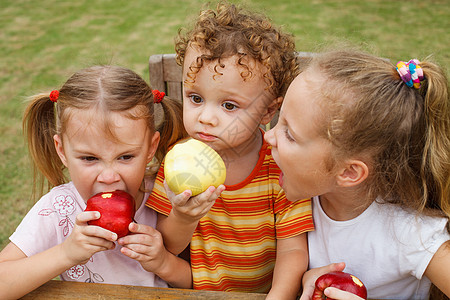 三个快乐的孩子坐在桌边吃苹果 坐着吃饭水果乐趣童年男生饮食公园幸福头发婴儿女孩图片
