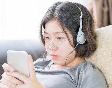 亚裔女性通过手机听音乐的女性青少年女孩沙发长椅歌曲收音机耳机寒意女士闲暇图片