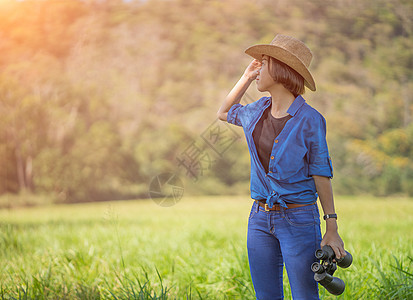 妇女戴帽子 在草地佩戴望远镜荒野森林女性女士农村绿色天空闲暇旅游监视图片