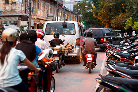 极限摩托车在柬埔寨暹粒的夜交通 汽车 骑自行车的男人 和滑稽的方式用自行车运送猪背景