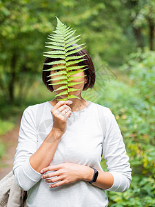 年轻女性用青叶遮住眼睛 象征着生命 安宁和与自然的团结 森林中的夏天手表植物生活叶子木头绿色蕨类森林统一休息图片