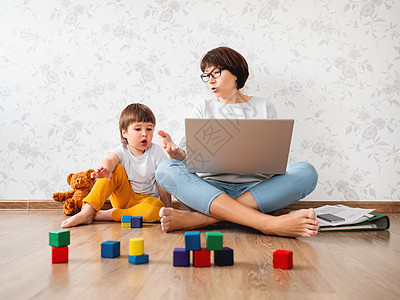 由于冠状病毒 COVID19 母子在家庭隔离中争吵 母亲远程使用笔记本电脑工作 儿子玩玩具积木 在家自我隔离婴儿技术男生地面封锁图片