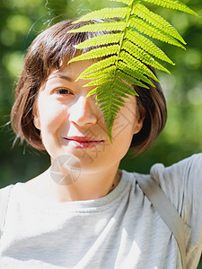 年轻女性用青叶遮住眼睛 象征着生命 宁静和与自然的团结 森林中的夏天统一叶子绿色生活隐藏植物蕨类木头幸福微笑图片