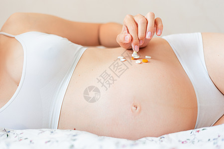 身穿白内裤的孕妇躺在床上 吃着许多药丸 年轻女性正在怀孕 必须服药药片卫生药品腹部药剂母性男生玩具药理婴儿图片