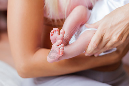 母亲拿着新生婴儿的赤身高跟鞋 小脚在女人手里 在家很舒服蓝色家庭女士白色脚跟手指女儿妈妈儿子父母图片