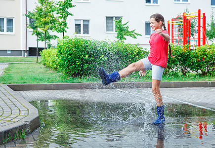 女孩穿着蓝色橡皮靴 在雨后在水坑里跳乐趣童年女士靴子季节下雨橡皮跳跃衣服短裤图片