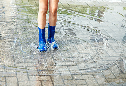 身穿蓝橡胶靴的女孩在雨后站在水坑里靴子衣服下雨天气乐趣蓝色女士童年季节孩子图片