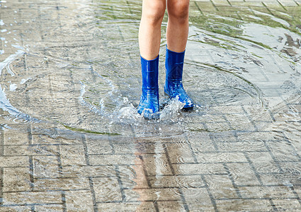 身穿蓝橡胶靴的女孩在雨后站在水坑里天气衣服孩子城市靴子橡皮女士童年街道季节图片